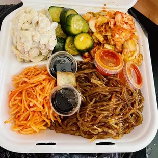 Ban Chan side dishes of long rice, Mac salad, shredded daikon, kimchi, and cucumbers.