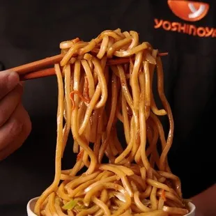 a person holding chopsticks over a bowl of noodles