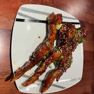 a plate of chicken wings with sesame seeds and scallions