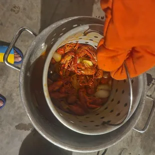 a person holding a colander full of crawfish