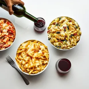three bowls of pasta and a bottle of wine