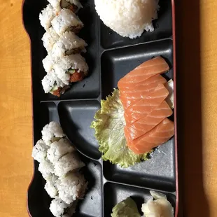 a tray of sushi with salmon, rice, and lettuce