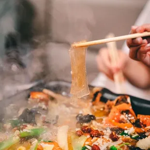 rson holding chopsticks over a pan of food