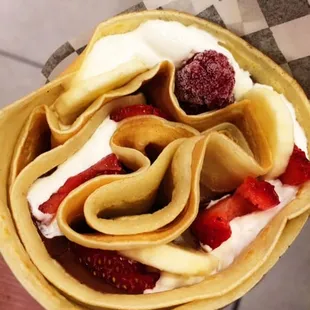 a person holding a crepe filled with strawberries and whipped cream