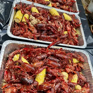 three trays of cooked crawfish and corn