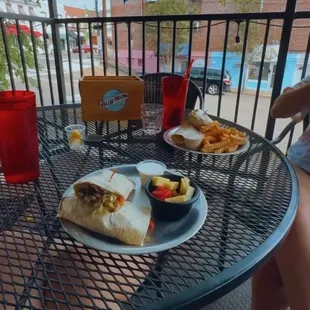cheesesteak wrap with fruit cup, and shrimp wrap with french fries; seated at a table in the patio dining