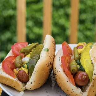 two hotdogs with pickles and tomatoes