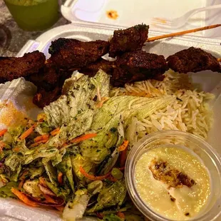 a plate of meat skewers, rice, and salad