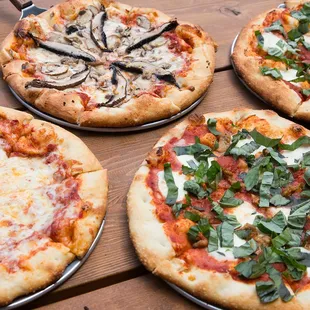 four different pizzas on a wooden table