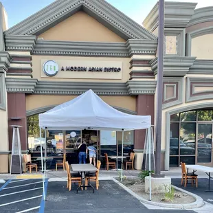 Outside: view of entrance and outdoor dining set up from parking lot