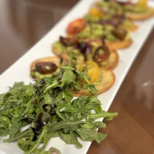 Avocado Toast, a harmonious blend of smashed avocado, heirloom tomatoes, arugula, pickled onion, and EVOO on garlic toast.