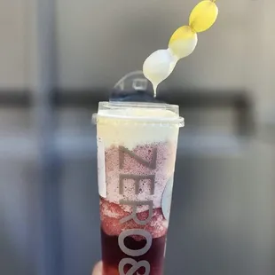  a hand holding a plastic cup filled with a drink and a spoon