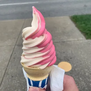 a hand holding a pink and white ice cream cone