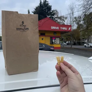 a hand holding a donut in front of a drive thru bag