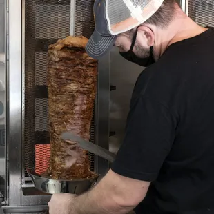 a man cutting a large meat on a skewer