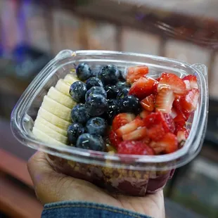a hand holding a container of fruit