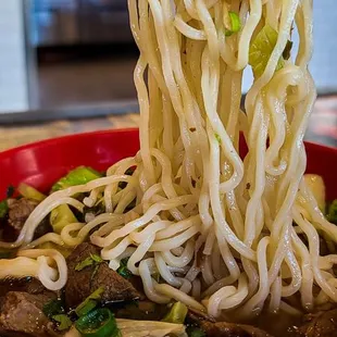 a bowl of noodles being lifted by chopsticks