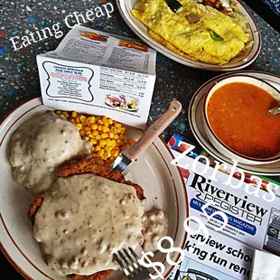 a plate of chicken fried steak with gravy and a bowl of soup