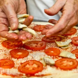 a person putting toppings on a pizza